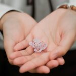 Close-up of hands gently holding a delicate pink flower symbolizing care and nature.